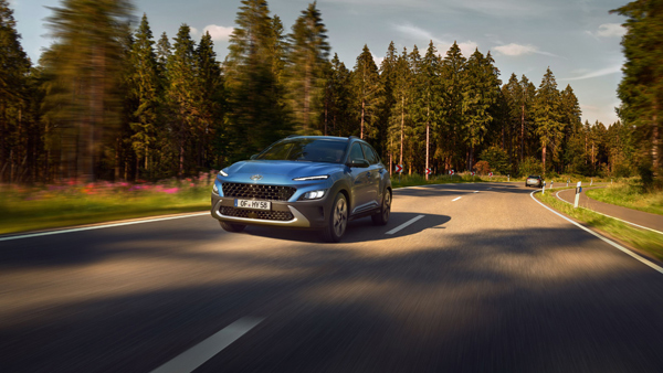 Pohled zepředu na nový Hyundai KONA v barvě Surfy Blue, jedoucí po polní cestě lesem.